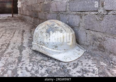 Scheußlicher Schutzhelm auf dem Boden, mit einem Spritzer Betonzement bedeckt, schwer überarbeitet Stockfoto