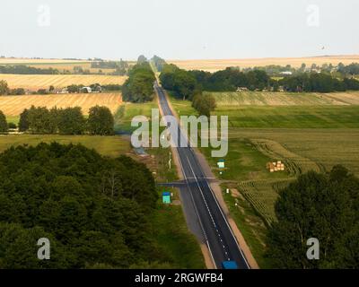 Landstraße zum Dorf zwischen Feldern vor blauem Himmel Stockfoto