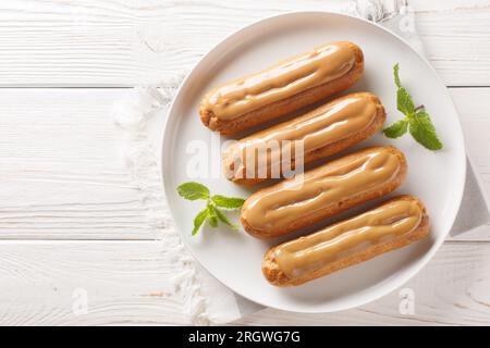 Traditionelle französische Dessert-Eclairs mit Vanillesauce und Karamellglasur in Nahaufnahme auf einem Teller auf dem Tisch. Horizontale Draufsicht von oben Stockfoto