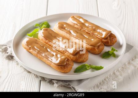 Exquisites Eclair mit cremiger Füllung und Nahaufnahme mit weichem, zartem Karamell auf einem Teller auf dem Tisch. Horizontal Stockfoto