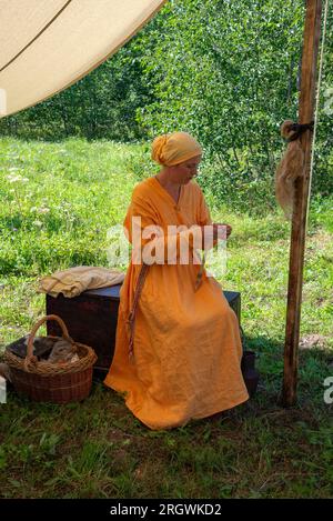 NOVGOROD REGION, RUSSLAND - 05. AUGUST 2023: Ein Mädchen in mittelalterlicher Kleidung, das Garn spinnt Stockfoto