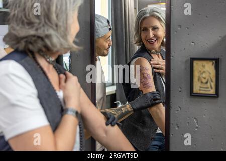 Eine langhaarige Frau, die in den Spiegel schaut und ihr neues Tattoo sieht Stockfoto