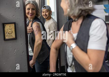 Eine langhaarige Frau, die in den Spiegel schaut und ihr neues Tattoo sieht Stockfoto