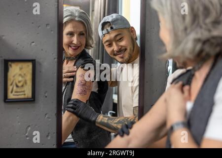 Eine langhaarige Frau, die in den Spiegel schaut und ihr neues Tattoo sieht Stockfoto