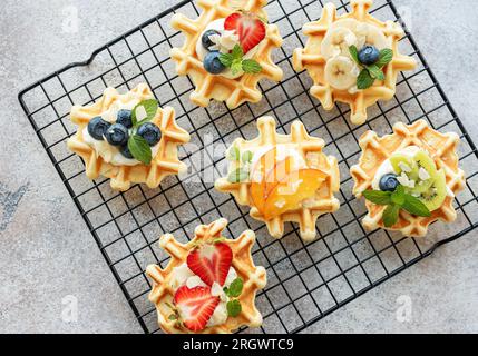Frisch gebackene Waffeln mit Erdbeeren und Blaubeeren auf Textilhintergrund. Hausgemachtes Backen. Stockfoto