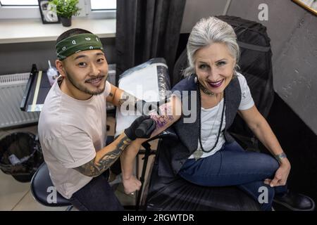 Männlicher Tätowierer, der mit einem Kunden im Salon arbeitet Stockfoto