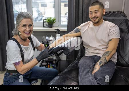 Der Tätowierer, der ein Tattoo für den männlichen Klienten macht Stockfoto