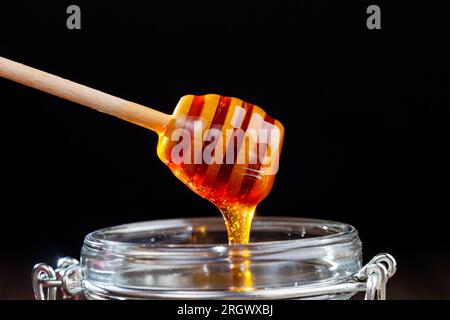 Fließend dicker und köstlicher süßer Honig fließt in ein Glasgefäß, ein natürliches und gesundes Nahrungsprodukt von Bienen, natürlicher Bienenhonig hat eine Viskose Stockfoto