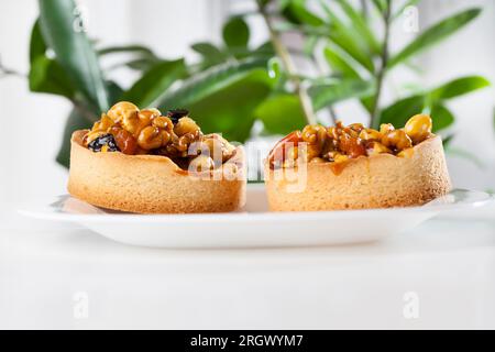 Verschiedene Nüsse in einem runden Törtchen, ein rundes Törtchen mit Nüssen und getrockneten Früchten, die mit Karamell gegossen werden, die Zutaten in dem zubereiteten Törtchen sind haselnussbraun Stockfoto