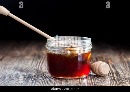 Ein Löffel für Honig zusammen mit hochwertigem Bienenhonig, ein alter Tisch, auf dem ein gesunder und süßer Bienenhonig steht, und ein spezieller Holzlöffel Stockfoto