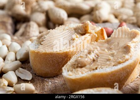 Nahaufnahme köstliche Erdnussbutter und Weißbrot auf dem Tisch, Zutaten für die Zubereitung eines schnellen Frühstücks mit Brot und Erdnüssen, Erdnusspaste geröstet p Stockfoto