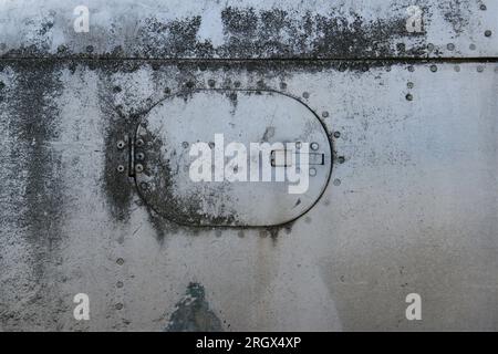 Ein Fragment eines alten Flugzeugrumpfes mit Nieten und einer Luke. Stockfoto