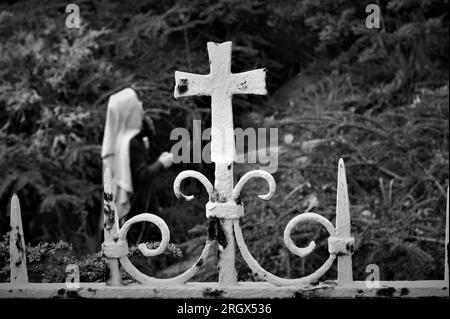 Ein Fragment eines alten Metallzauns. Alter Metallzaun mit einem Kreuz in der Nähe der Kirche. Schwarzweißbild. Stockfoto