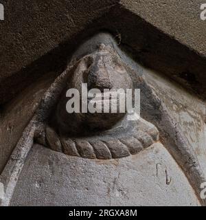 Rätselhaftes Gesicht aus der frühen normannischen Zeit, gemeißelt in die Hauptstadt der Säule, die den Kanzelbogen in der Pfarrkirche St. Nikolaus in Bramber in West Sussex, England, unterstützt. Die Kirche wurde 1073 gegründet und gilt als eine von drei Kirchen in ganz England mit originalen normannischen Schnitzereien aus dem 11. Jahrhundert auf Kanzelbogensäulen. Stockfoto