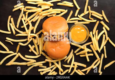 Zwei Cheeseburger, Pommes frites auf einem dunklen Holztisch und Senf, Blick von oben. Köstliches Fast Food. Burger Stockfoto