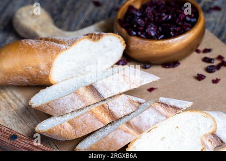 Cranberry und schneiden Sie frisches Weizen-Baguette in mehrere Stücke, schneiden Sie weiches frisches Baguette auf einem Schneidebrett und einem Tisch Stockfoto