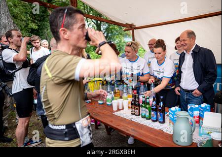 Teltow, Deutschland. 12. Aug. 2023. Bundeskanzler Olaf Scholz (SPD) besucht eine Erfrischungsstation des Berliner Wall Trail Run. Seit 2011 gedenkt der Wall Trail Run den Opfern der innerdeutschen Grenze. Die Fahrt findet entlang des ehemaligen Grenzstreifens statt. Kredit: Fabian Sommer/dpa/Alamy Live News Stockfoto