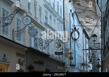 Alte, traditionelle, schmiedeeiserne Schilder hängen über den Geschäften in der Getreidegasse - einer berühmten Einkaufsstraße in der Altstadt von Salzburg Stockfoto