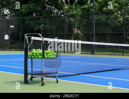 Nahaufnahme eines blauen Tennisplatzes mit einem Wagen, der viele Tennisbälle neben dem Netz hält, um zu üben. Stockfoto