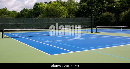 Weiter Blick auf zwei blaue und grüne Tennisplätze, die auch für Pickleball-Spiele gesäumt sind. Stockfoto