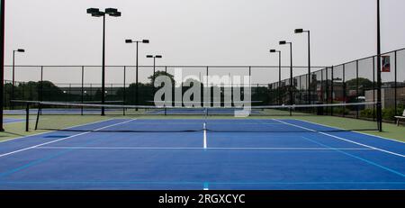 Vorderansicht der blauen und grünen Tennisplätze mit Lichtern, umgeben von hohen schwarzen Zäunen. Stockfoto
