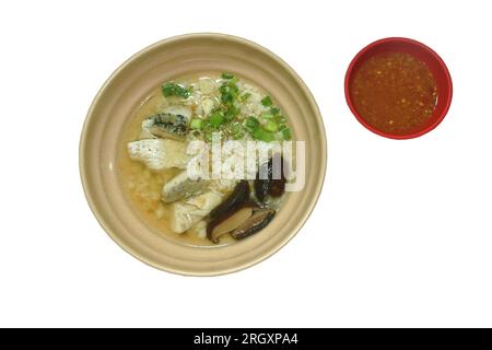 Gekochter Reis mit einer Scheibe Barschfisch mit hackigen Frühlingszwiebeln und gebratenem Knoblauch in einer klaren Suppe auf einer Schüssel mit würziger Chilisauce Stockfoto