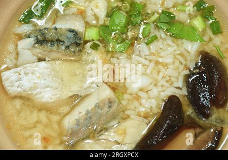 Gekochter Reis mit einer Scheibe Barschfisch mit hackigen Frühlingszwiebeln und gebratenem Knoblauch in einer klaren Suppe auf einer Schüssel mit würziger Chilisauce Stockfoto