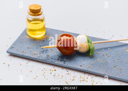 Kirschtomaten, Mozzarella-Käse und Basilikumblätter auf einem Spieß und einem Glas mit nativem Olivenöl extra. Stockfoto