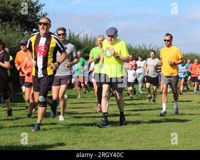 Kesgrave, Suffolk - 12. August 2023 : Kesgrave's 400. Park Run Event auf dem Millennium Field. Ein älterer Mann mit einer flachen Mütze, der stark läuft. Stockfoto