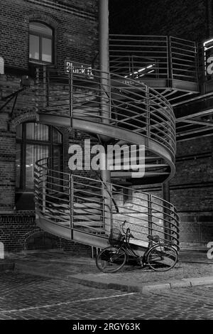 Hamburg - Juni 16 2023: Wendeltreppe und altes Fahrrad im Lagerbezirk Speicherstadt in Schwarz und Weiß. Stockfoto