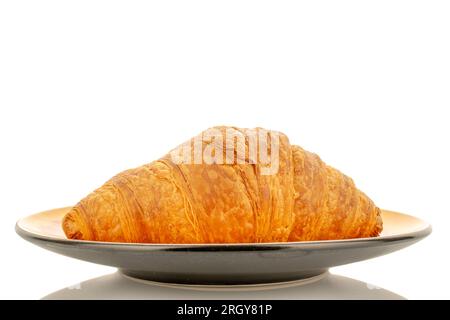 Ein frisch gebackenes, duftendes Croissant auf einer Untertasse, Nahaufnahme, isoliert auf Weiß. Stockfoto