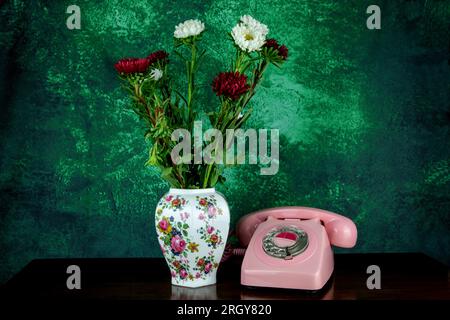 Telefon in Vintage-Pink mit Blumenvase auf einem polierten Holztisch Stockfoto