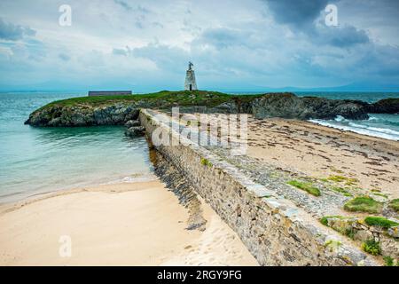 Little Lighthouse Llanddwyn Island Anglesey an einem stimmungsvollen Wettertag, an dem die Hafenmauer als todale Barriere dient. Llanddwyn ist eine Gezeiteninsel Stockfoto