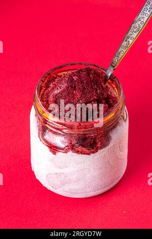 Hausgemachte Heidelbeersorbet-Granita mit Blaubeerfrucht in heiterfrostem Glasglas auf rotem Hintergrund. Sommerdessert, süßer Snack. Stockfoto