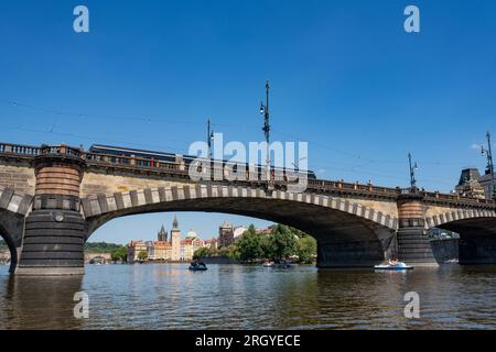 „Most Legií“ (Legionsbrücke) über der Moldau in Prag. Die Trampbahn überquert die Brücke, den Gebäudekomplex „Karlovy Lázně“ im Hintergrund. Stockfoto