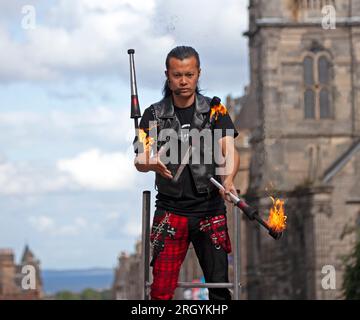 Royal Mile, Edinburgh, Schottland, Großbritannien. 12. August 2023. Edinburgh Festival Fringe, Straßenkünstler in der High Street, die vor einem großen Publikum auftreten, windig für Jonglierende mit Feuer und auf Plattformen, Sonnenschein und gelegentlich heftige Duschen. Abbildung: Showtime für Kozo Kaos, während er auf der High Street mit Fackeln im Wind jongliert. Kredit: Archwhite/alamy Live News. Stockfoto