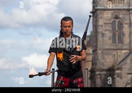 Royal Mile, Edinburgh, Schottland, Großbritannien. 12. August 2023. Edinburgh Festival Fringe, Straßenkünstler in der High Street, die vor einem großen Publikum auftreten, windig für Jonglierende mit Feuer und auf Plattformen, Sonnenschein und gelegentlich heftige Duschen. Abbildung: Showtime für Kozo Kaos, während er auf der High Street mit Fackeln im Wind jongliert. Kredit: Archwhite/alamy Live News. Stockfoto