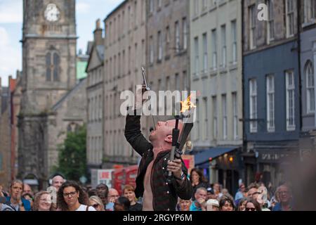 Royal Mile, Edinburgh, Schottland, Großbritannien. 12. August 2023. Edinburgh Festival Fringe, Straßenkünstler in der High Street, die vor einem großen Publikum auftreten, windig für diejenigen, die mit dem Feuer jonglieren und auf Plattformen, Sonnenschein und gelegentlich heftiger Dusche. Abbildung: Straßenkünstler Tommy führt sein Schwert-Awalloing auf der High Street auf. Kredit: Archwhite/alamy Live News. Stockfoto