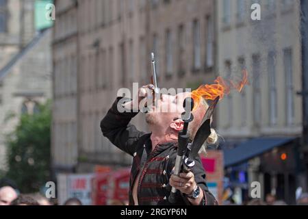 Royal Mile, Edinburgh, Schottland, Großbritannien. 12. August 2023. Edinburgh Festival Fringe, Straßenkünstler in der High Street, die vor einem großen Publikum auftreten, windig für diejenigen, die mit dem Feuer jonglieren und auf Plattformen, Sonnenschein und gelegentlich heftiger Dusche. Abbildung: Straßenkünstler Tommy führt sein Schwert-Awalloing auf der High Street auf. Kredit: Archwhite/alamy Live News. Stockfoto