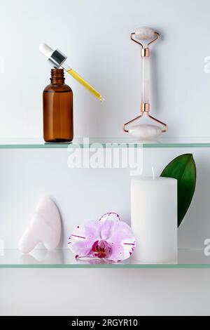 Serumflasche aus Glas mit Pipette, Duftkerze im Badezimmer. Gua-Sha-Massagewerkzeug. Natürliches Öl. Orchideenblume. Spa-Behandlungen und Schönheitsbehandlungen. An Stockfoto