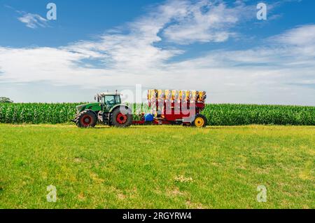 Landmaschinen fahren über das Feld. Großer Traktor. Sider-Ansicht. Weiße Kumuluswolken im Hintergrund Stockfoto