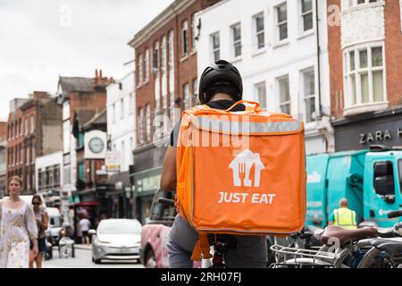 Ein Fahrer, der mit einer großen Orange auf seinem Fahrrad sitzt, isst einen isolierten Rucksackbehälter, der auf seinem Rücken ruht. Richmond, Surrey Stockfoto