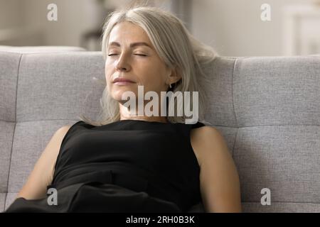 Friedliche, entspannte, reife Dame, die zu Hause auf einer gemütlichen Couch schläft Stockfoto