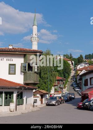 Restaurant Inat Kuca mit einem Minarett dahinter und einer steilen Straße voller Autos, die am 12. August 2023 in Sarajevo, Bosnien und Herzegowina, geparkt wurden. Stockfoto