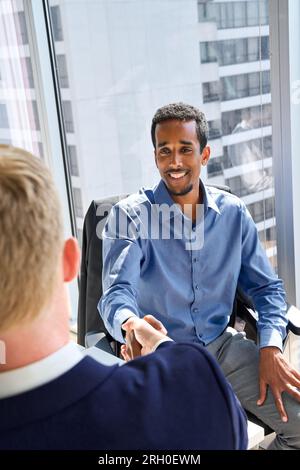Vielfältige, glückliche Geschäftsmänner, die sich bei der Bürobesprechung die Hand schütteln. Vertikal Stockfoto