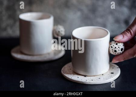 Handgemachte Kaffeetassen mit Punktmuster und Frauenhand auf dunklem Hintergrund, Nahaufnahme Stockfoto