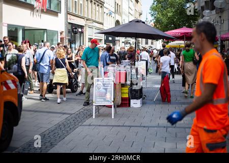 München, Deutschland. 12. Aug. 2023. Müllsammelarbeiter leert Mülltonnen. Neben ihm ein Stand der Scientologie am 12. August 2023 in München. (Foto: Alexander Pohl/Sipa USA) Guthaben: SIPA USA/Alamy Live News Stockfoto