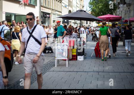 München, Deutschland. 12. Aug. 2023. Müllsammelarbeiter leert Mülltonnen. Neben ihm ein Stand der Scientologie am 12. August 2023 in München. (Foto: Alexander Pohl/Sipa USA) Guthaben: SIPA USA/Alamy Live News Stockfoto