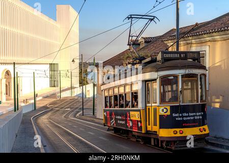 Lissabon, Portugal. Straßenszene mit Straßenbahn in Calcada da Ajuda. Die moderne Fassade des Palacio National de Ajuda im Hintergrund. Stockfoto