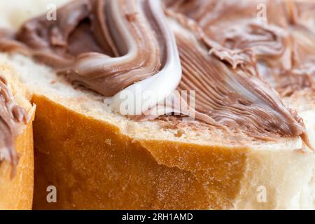 Frisches, weiches Baguette in Stücke schneiden und mit Schokoladencreme, Schokoladenpaste auf einem weißen Weizenbaguette verteilen Stockfoto